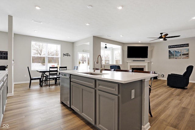 kitchen featuring ceiling fan, stainless steel dishwasher, gray cabinetry, light countertops, and a sink
