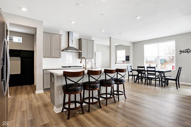 kitchen featuring a breakfast bar area, gray cabinetry, a center island with sink, and wall chimney exhaust hood
