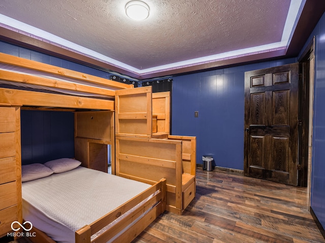 bedroom with a tray ceiling, dark wood-type flooring, and a textured ceiling