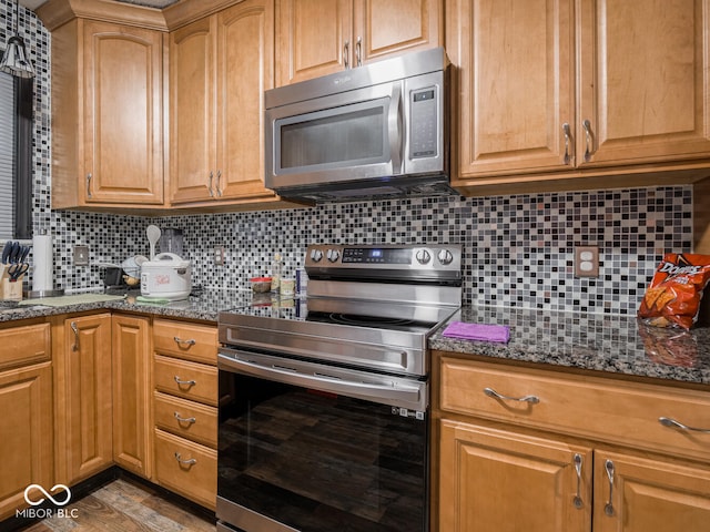 kitchen with decorative backsplash, light hardwood / wood-style flooring, dark stone counters, and appliances with stainless steel finishes