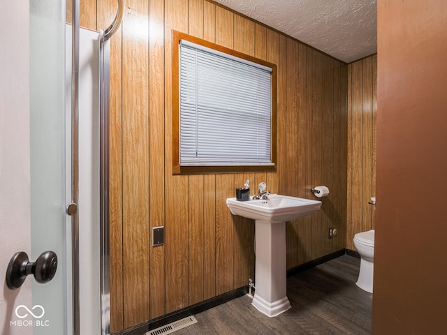 bathroom with sink, hardwood / wood-style floors, a textured ceiling, toilet, and wood walls