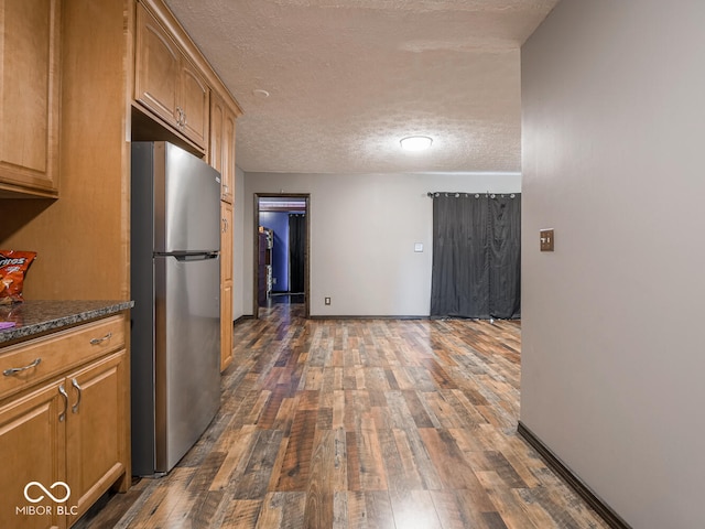 kitchen featuring dark stone countertops, dark hardwood / wood-style floors, stainless steel refrigerator, and a textured ceiling