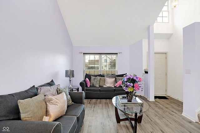 living room with high vaulted ceiling, baseboards, a healthy amount of sunlight, and light wood finished floors