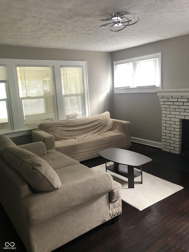 living room with wood-type flooring, a brick fireplace, and a textured ceiling