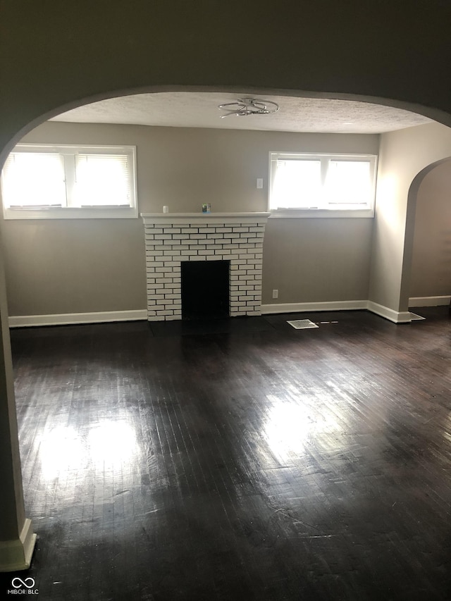 unfurnished living room featuring dark wood-type flooring, a healthy amount of sunlight, a fireplace, and a textured ceiling