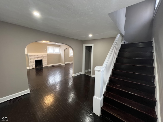 stairs with arched walkways, a textured ceiling, baseboards, and hardwood / wood-style floors