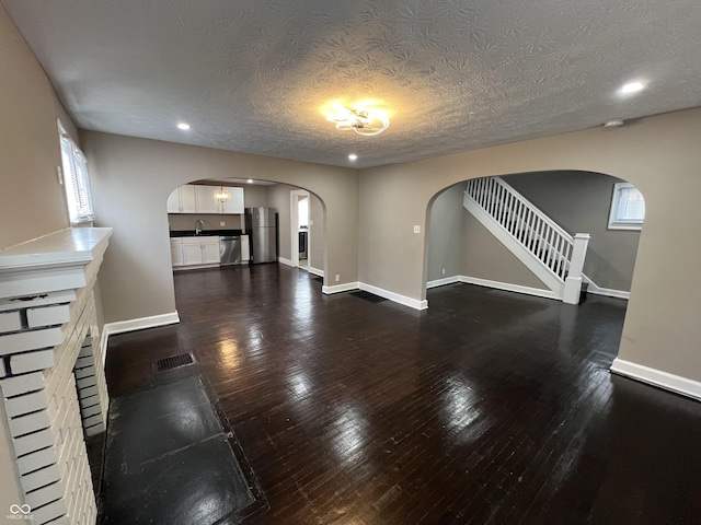 unfurnished living room featuring arched walkways, visible vents, baseboards, and dark wood-style flooring