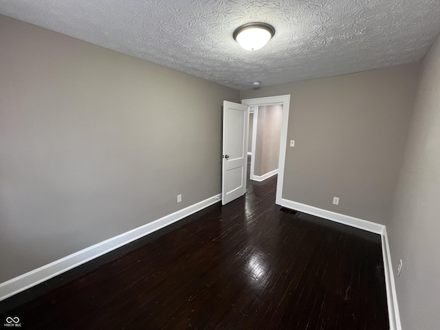 spare room featuring dark wood-type flooring, visible vents, baseboards, and a textured ceiling