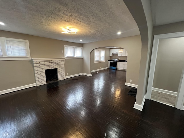 unfurnished living room featuring baseboards, arched walkways, and dark wood-style floors
