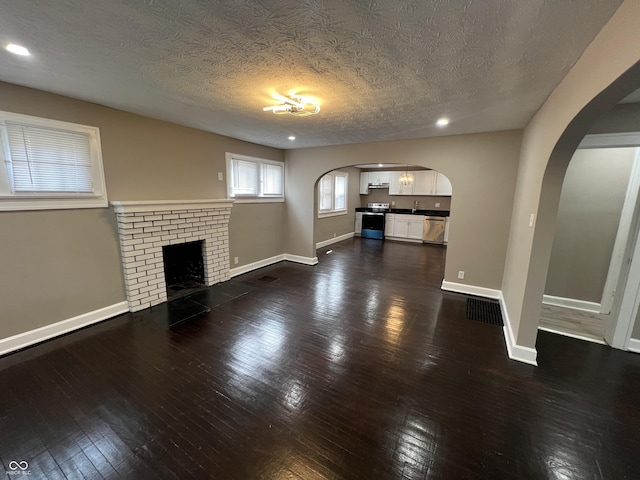 unfurnished living room with a brick fireplace, baseboards, arched walkways, and dark wood-style flooring