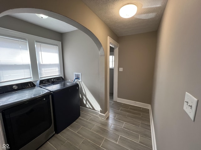 clothes washing area featuring baseboards, laundry area, arched walkways, independent washer and dryer, and a textured ceiling