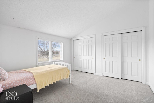 carpeted bedroom featuring vaulted ceiling, a textured ceiling, baseboards, and multiple closets