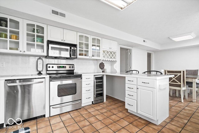 kitchen featuring wine cooler, stainless steel appliances, a peninsula, visible vents, and decorative backsplash