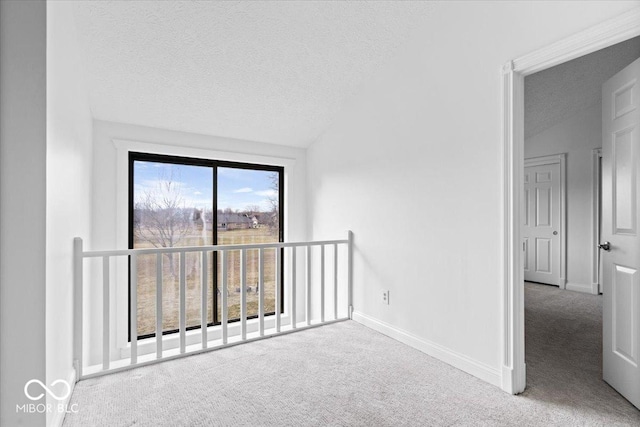 empty room featuring a textured ceiling, vaulted ceiling, carpet flooring, and baseboards