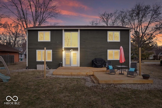 rear view of house with a playground, a lawn, and a wooden deck