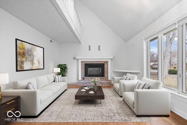 living room with lofted ceiling, a brick fireplace, visible vents, and wood finished floors