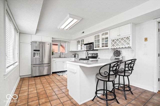 kitchen with stainless steel appliances, a peninsula, a sink, a kitchen breakfast bar, and glass insert cabinets