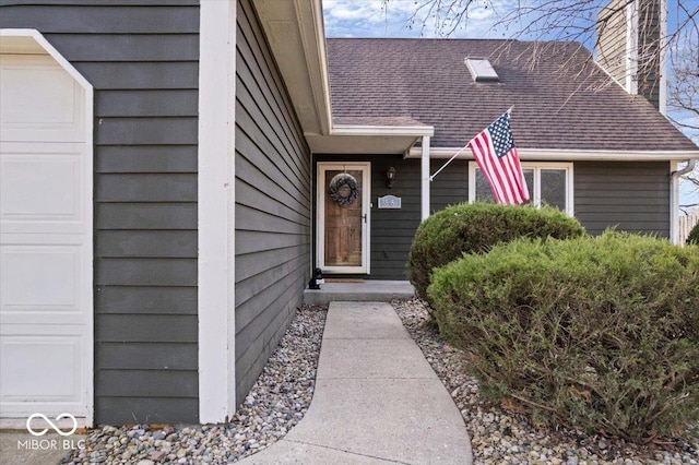 entrance to property featuring a garage and roof with shingles