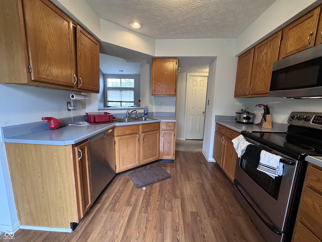 kitchen featuring a sink, light countertops, dark wood-type flooring, appliances with stainless steel finishes, and brown cabinetry