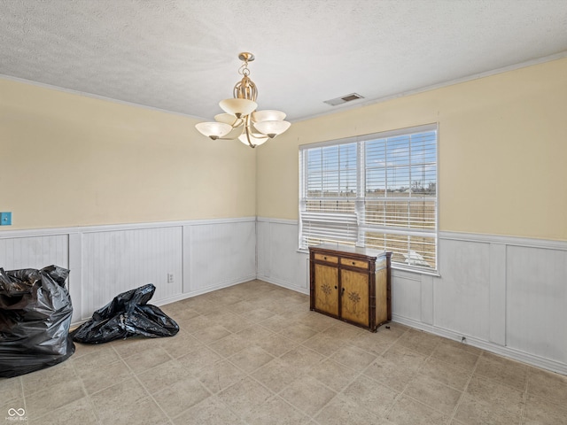 empty room featuring a chandelier, visible vents, wainscoting, and a textured ceiling