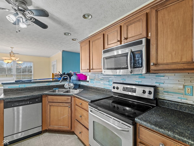 kitchen featuring dark countertops, appliances with stainless steel finishes, brown cabinets, and a sink