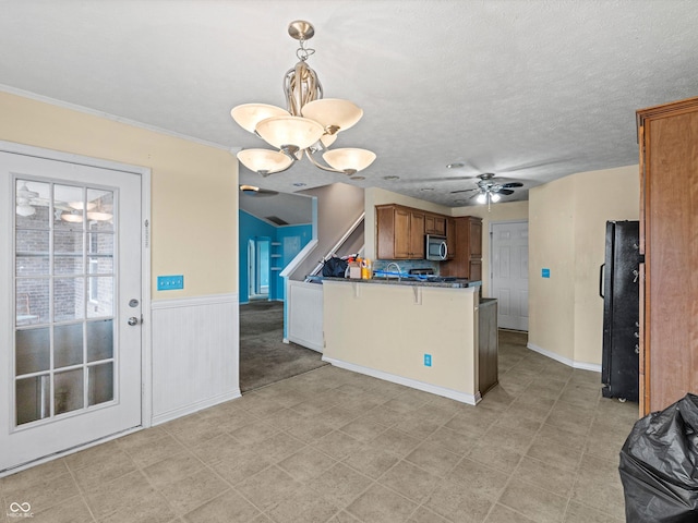 kitchen featuring dark countertops, stainless steel microwave, brown cabinets, freestanding refrigerator, and a peninsula