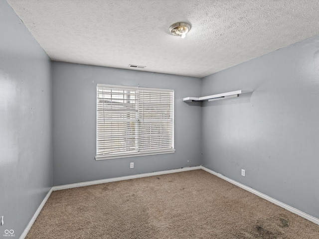 carpeted empty room with visible vents, a textured ceiling, and baseboards