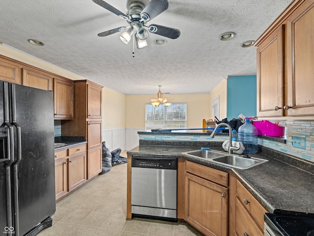 kitchen with dark countertops, a wainscoted wall, appliances with stainless steel finishes, and a sink