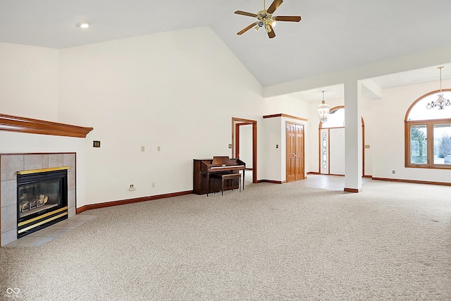 unfurnished living room with ceiling fan with notable chandelier, high vaulted ceiling, a tile fireplace, and carpet