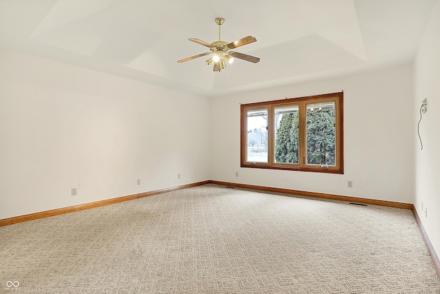 empty room with a raised ceiling, carpet floors, and ceiling fan