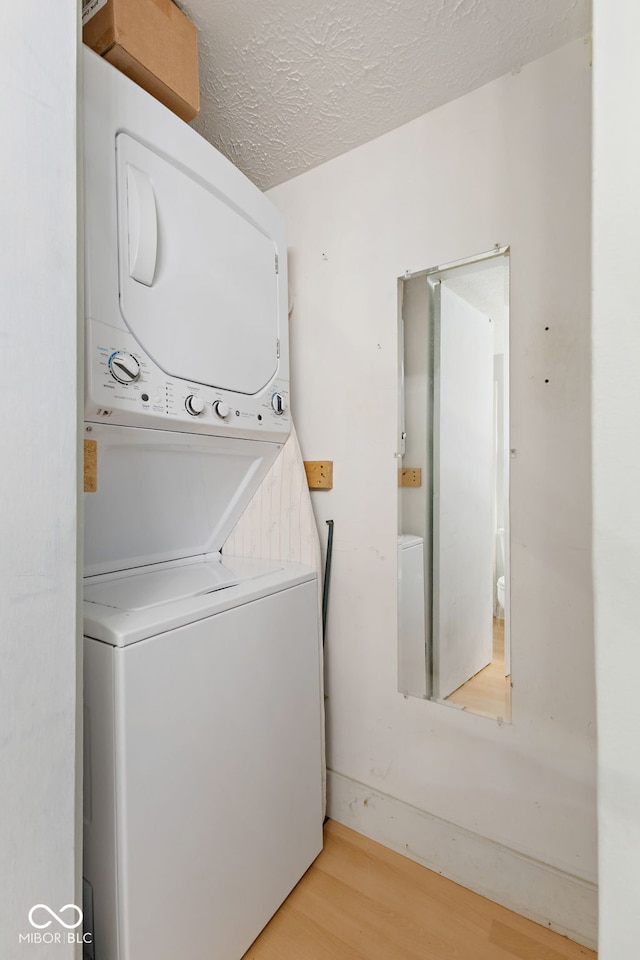 laundry area with stacked washer / drying machine, light hardwood / wood-style floors, and a textured ceiling