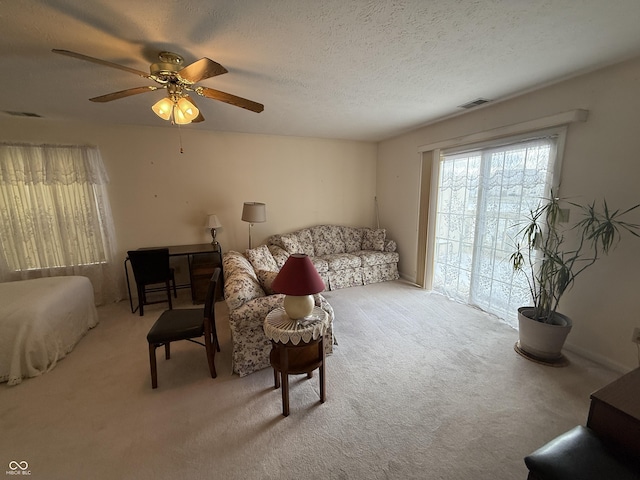 living room featuring light carpet, a ceiling fan, visible vents, and a textured ceiling