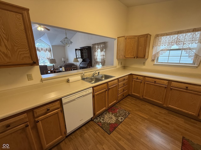 kitchen with brown cabinets, white dishwasher, vaulted ceiling, light countertops, and a sink