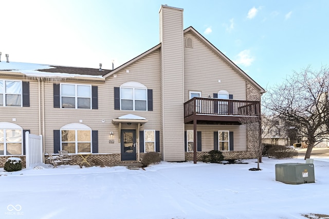 multi unit property with a balcony, a chimney, and brick siding