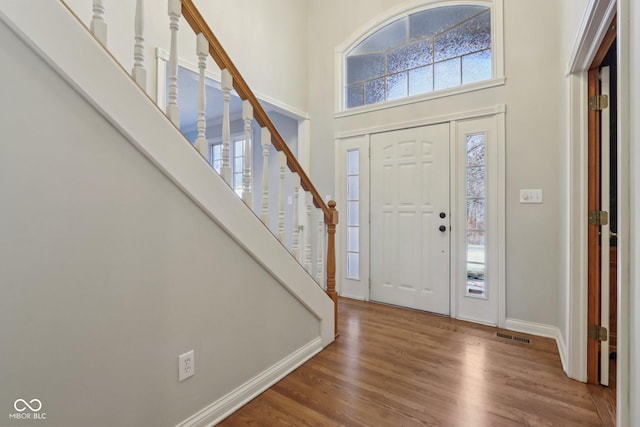 foyer entrance featuring visible vents, baseboards, stairway, a high ceiling, and wood finished floors