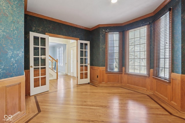 spare room with wallpapered walls, stairs, french doors, wainscoting, and light wood-type flooring