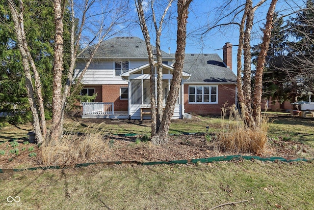 view of front of house with a wooden deck, a sunroom, a chimney, a front lawn, and brick siding