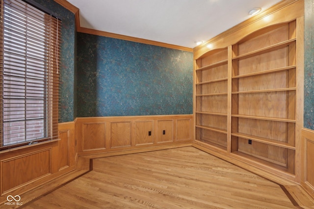 empty room with wallpapered walls, crown molding, a wainscoted wall, and light wood-type flooring