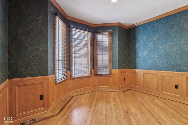 unfurnished room with visible vents, light wood finished floors, a wainscoted wall, and wallpapered walls