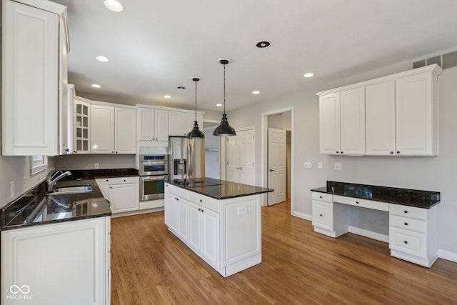 kitchen with a sink, light wood-style floors, appliances with stainless steel finishes, and built in desk