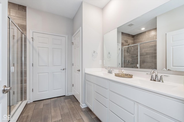 full bathroom featuring double vanity, a stall shower, wood tiled floor, and a sink