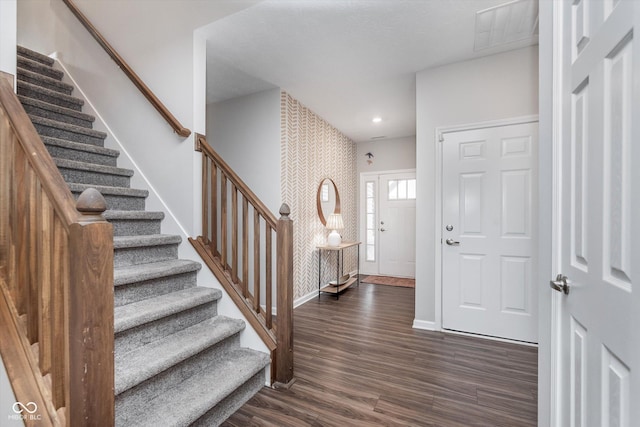 foyer with dark wood finished floors, visible vents, an accent wall, baseboards, and wallpapered walls