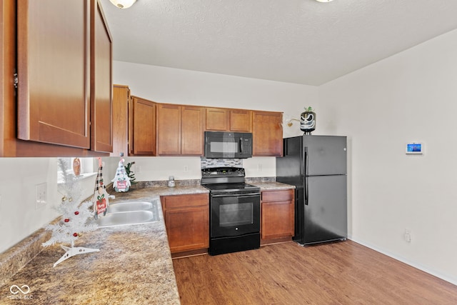 kitchen with sink, light hardwood / wood-style flooring, black appliances, and a textured ceiling