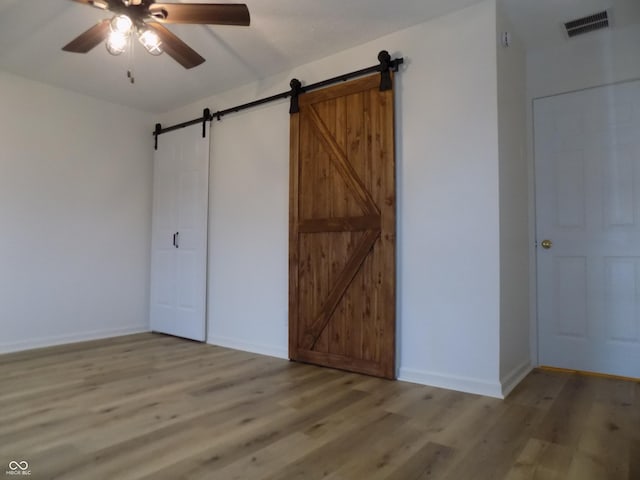 unfurnished bedroom featuring light wood-type flooring, ceiling fan, and a barn door