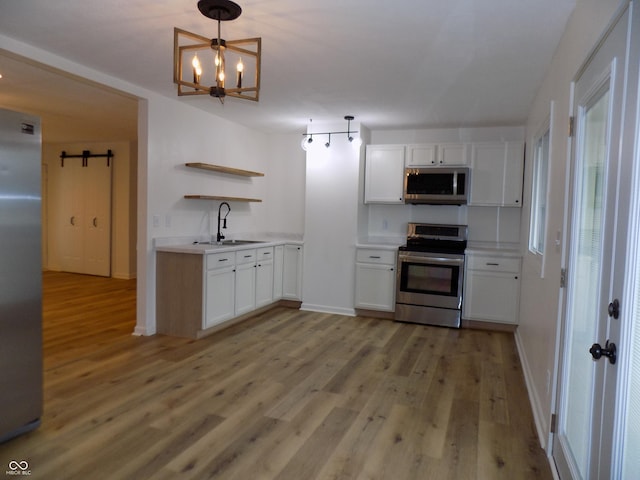 kitchen featuring appliances with stainless steel finishes, hanging light fixtures, light hardwood / wood-style floors, sink, and white cabinetry