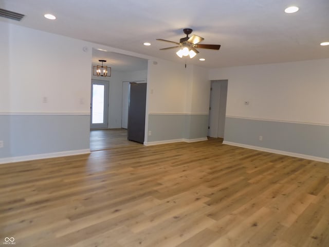 spare room featuring ceiling fan with notable chandelier and light wood-type flooring