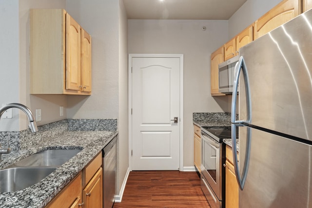 kitchen with sink, appliances with stainless steel finishes, dark stone counters, and dark hardwood / wood-style flooring