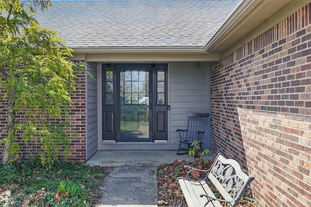property entrance with roof with shingles and brick siding