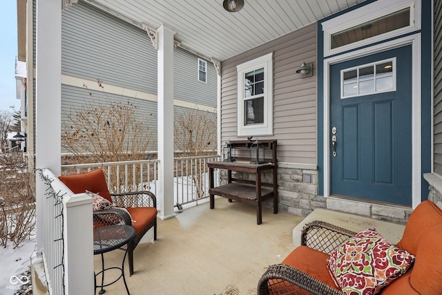 snow covered property entrance with stone siding and a porch