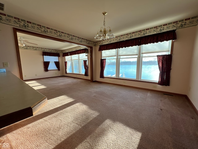 empty room with carpet, a water view, and a notable chandelier